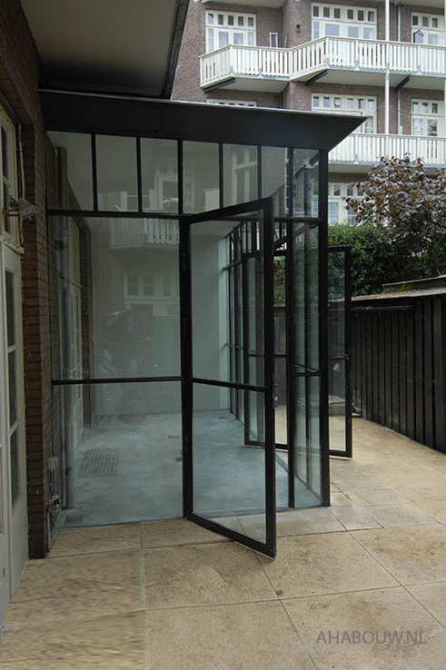 Taatsdeur en gewone deur in glas staal gevel aanbouw.